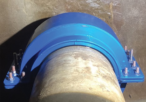 Herstelde leiding met nieuwe blauwe halfronde reparatieklem stevig gemonteerd rond de buis.